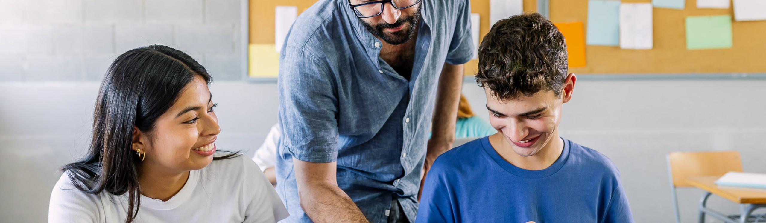 A male teacher helping two high school students on a project in a classroom