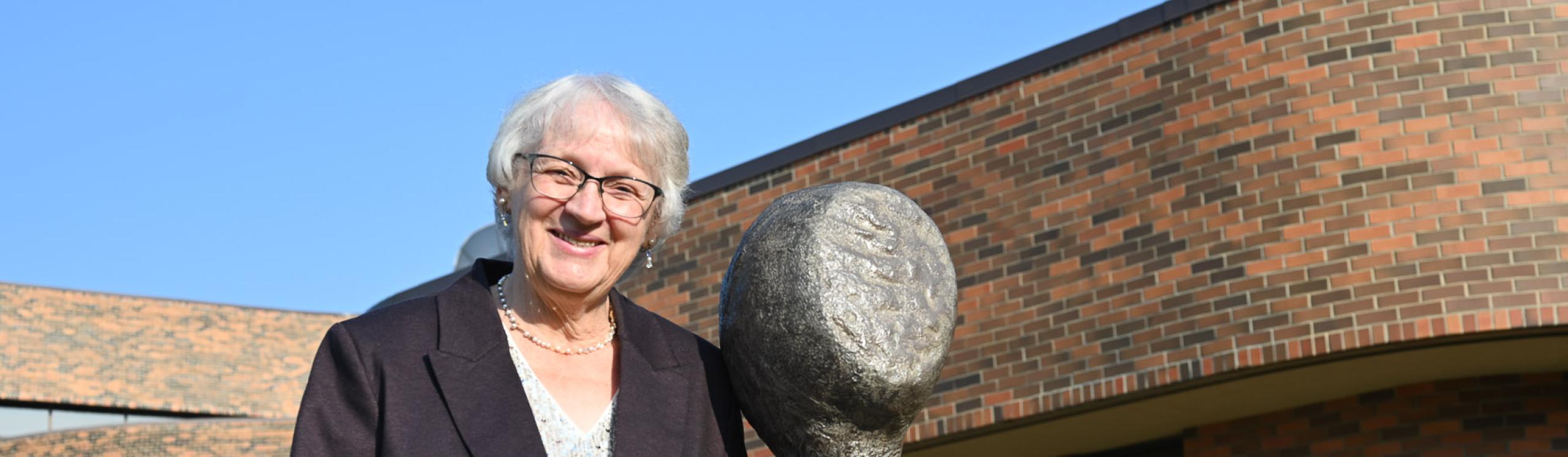 Helena Peters Mulligan standing beside one of her sculptures that stand at the main entrance of the Grande Prairie campus