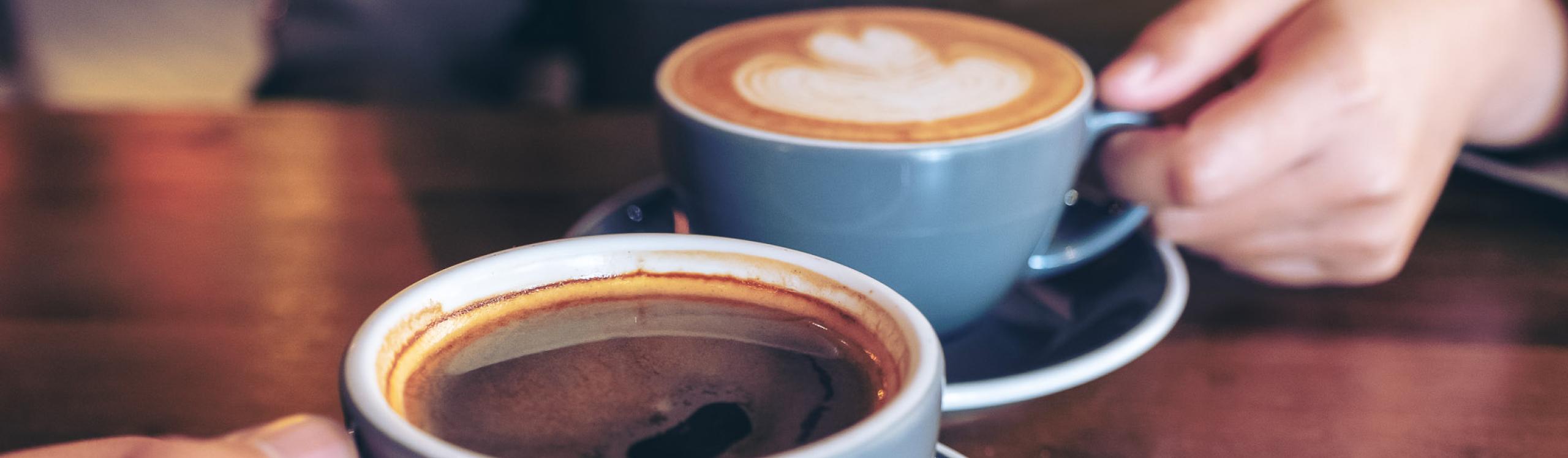 Close up image of a man and a woman clinking blue coffee mugs on wooden table in cafe