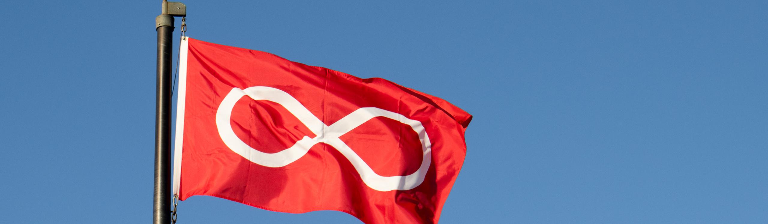 Red Metis flag flying against a bright blue sky