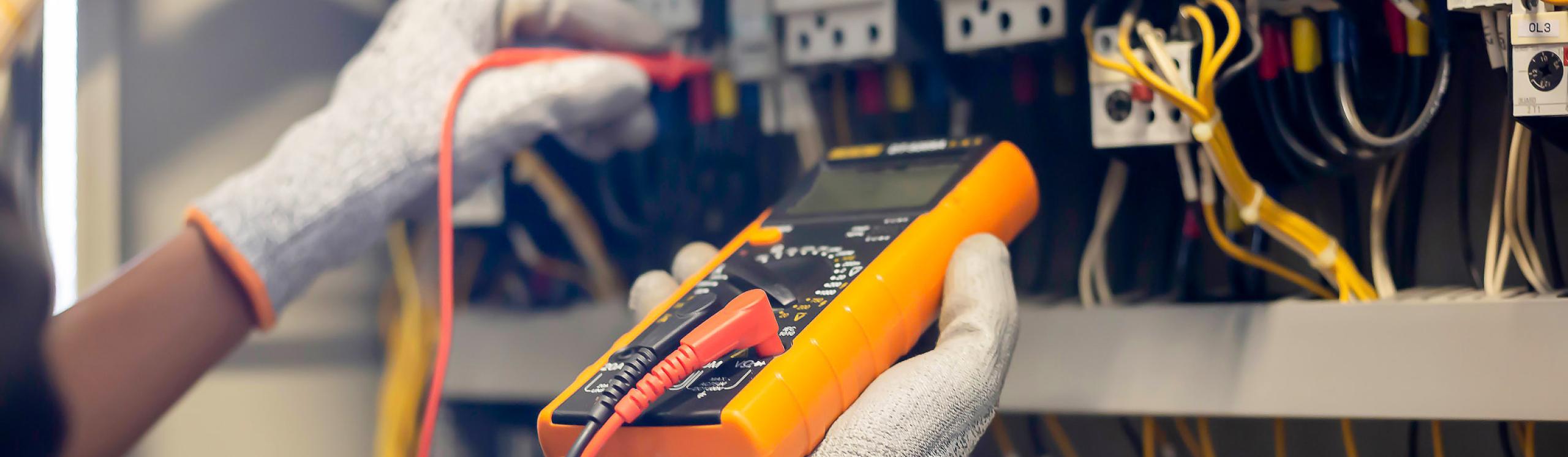 Electrician engineer uses a multimeter to test the electrical installation and power line current in an electrical system control cabinet.
