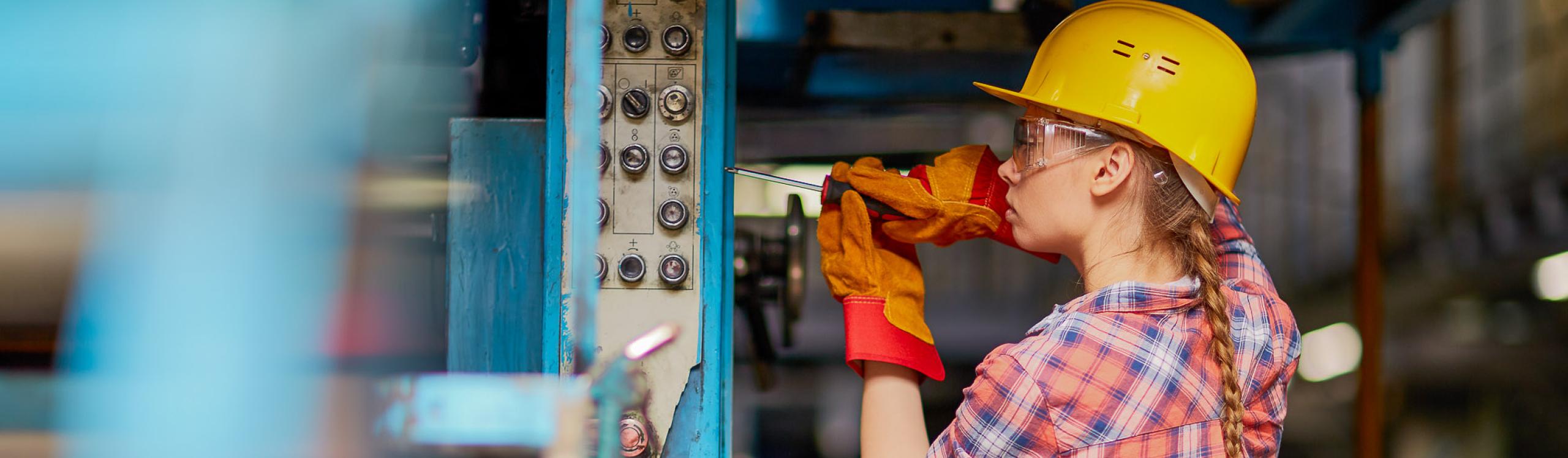 A skilled trades technician wearing safety gear works on a piece of equipment