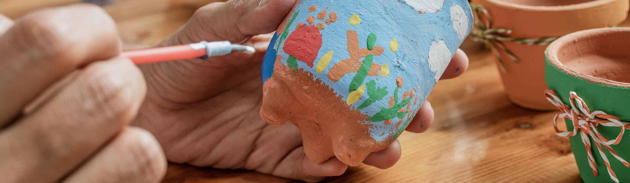 Close up shot of a person painting a colourful picture onto a clay pot