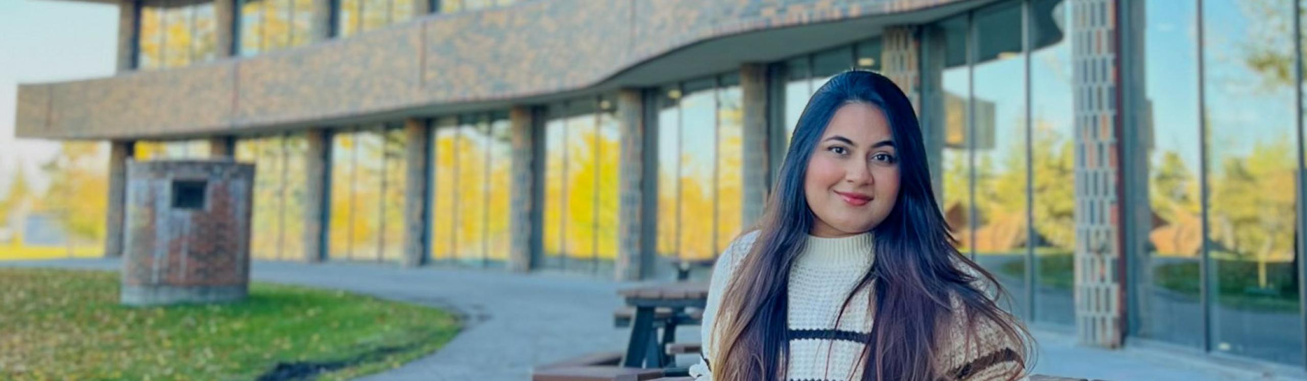 Busayna sitting on a bench on a clear summers aday with the NWP Cardinal building in the background