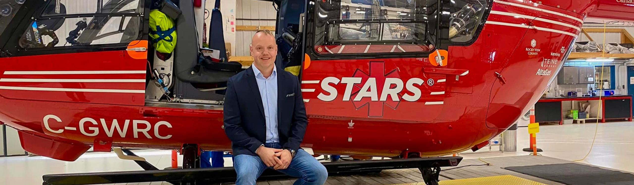 Shawn Shmyr seated at the entrance to the cabin of a bright red STARS helicopter