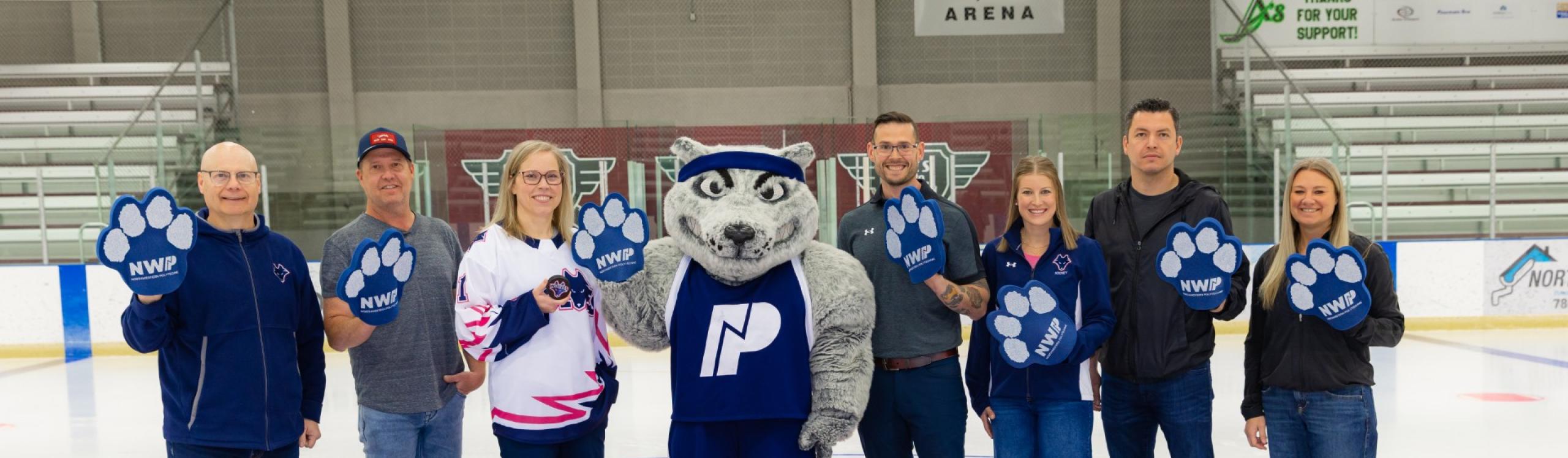 NWP and PCFAC leadership standing on centre ice at the Design Works arena waving giant foam wolf paws