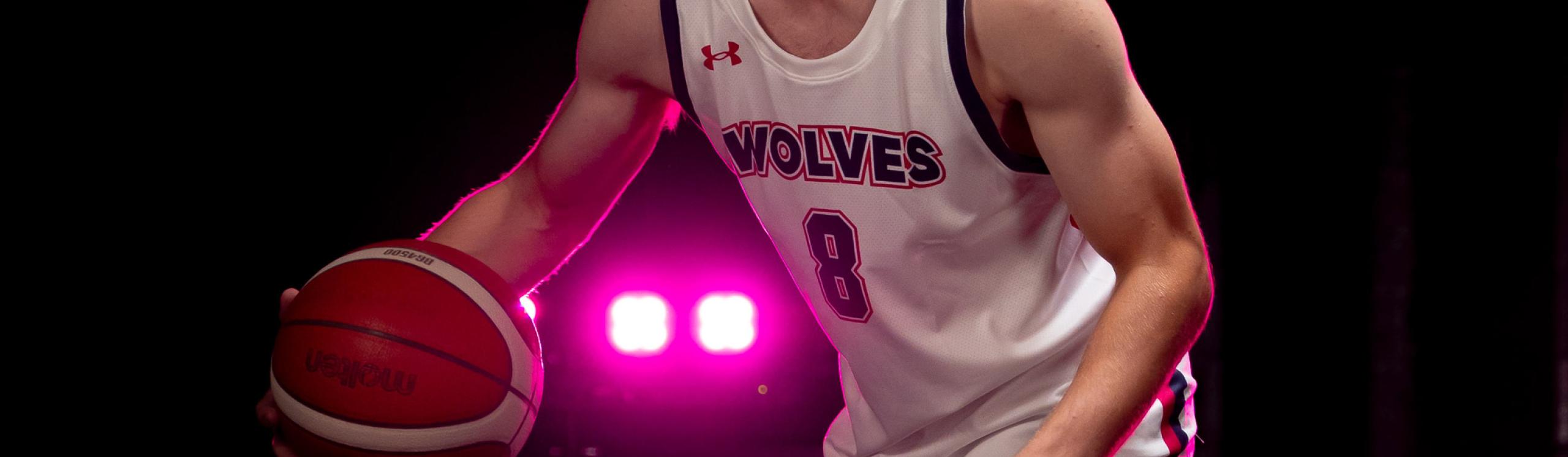 A close-up of the Wolves basketball crest on an athlete's jersey, highlighted by a vivid pink spotlight in the background.