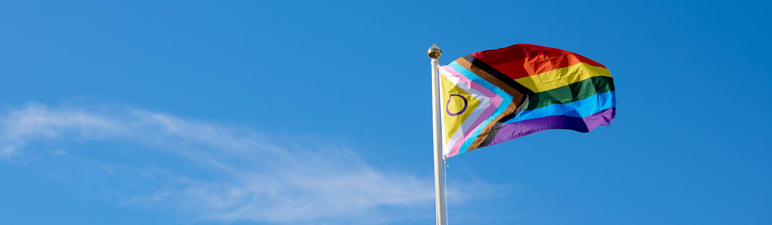Pride progress flag flying against a clear blue sky