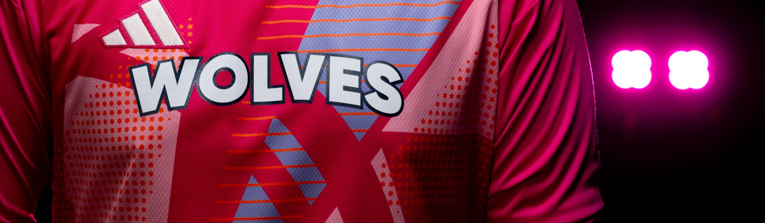 A close-up of the Wolves soccer crest on a goalkeeper's jersey, highlighted by a vivid pink spotlight in the background.