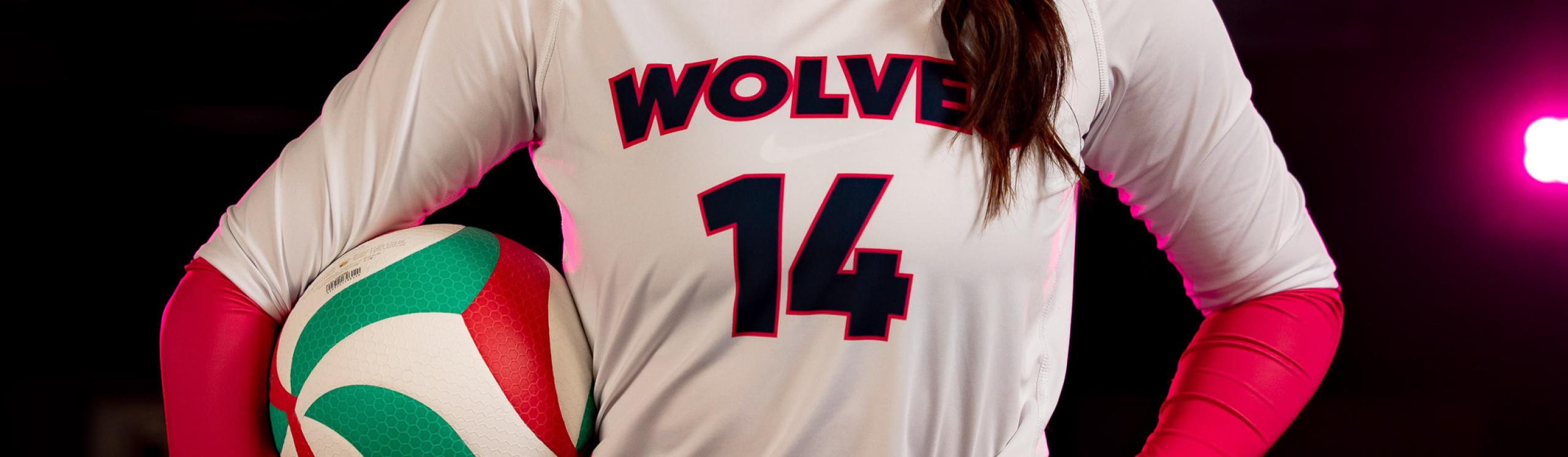 A close-up of the Wolves volleyball number and crest on an athlete's jersey, highlighted by a vivid pink spotlight in the background.