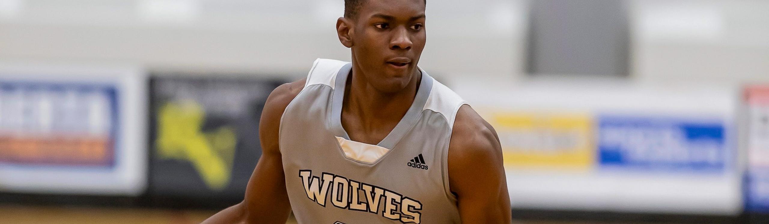 Manny Iloka wearing his #20 jersey while dribbling the ball on the basketball court
