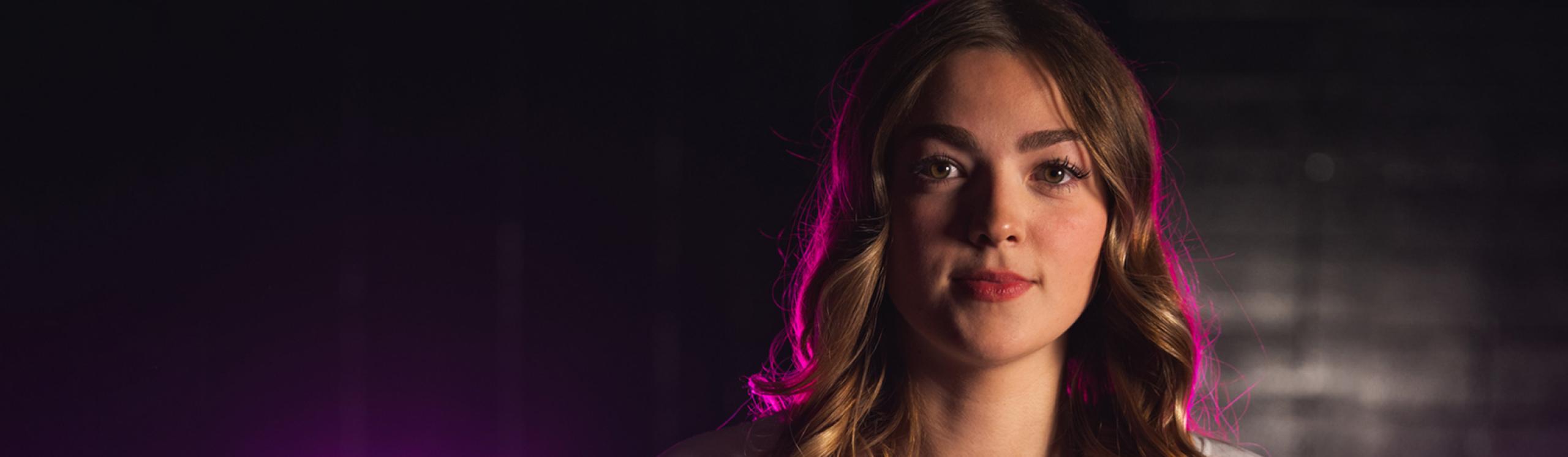Jaida Klimach posing in her team jersey. Pink lights shine brightly behind her. 